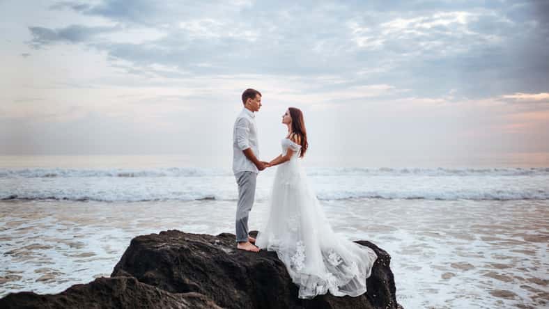 Elegant gorgeous bride and groom walking on ocean beach during sunset time. Romantic walk newlyweds on tropical island. Concept marriage, just married