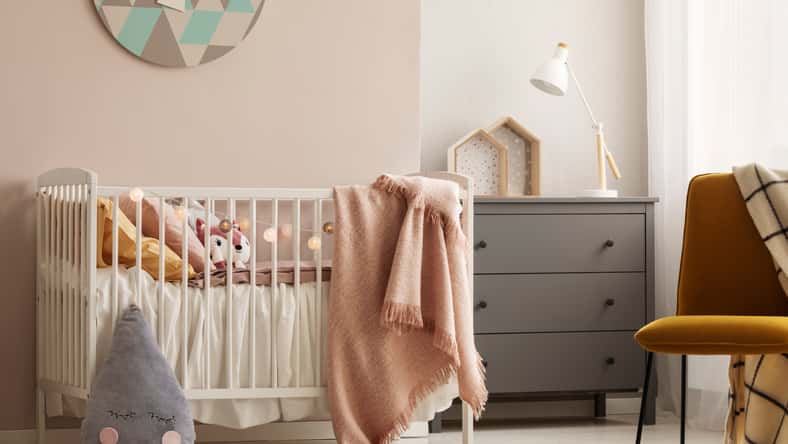 Pillows and toy in white wooden crib with pastel pink blanket in bright nursery