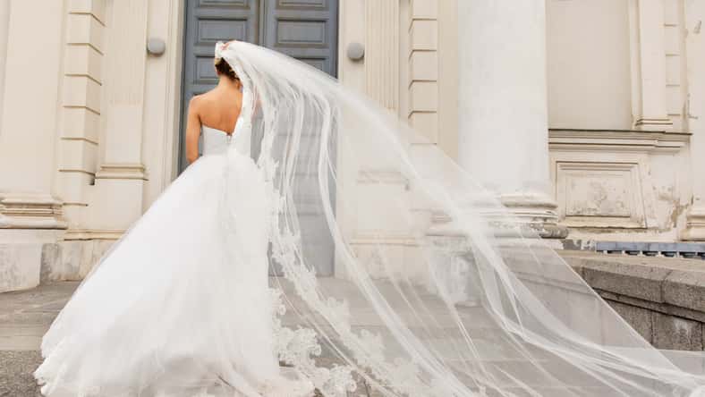 Wedding day. Bride in white wedding dress holding long veil with embroidery