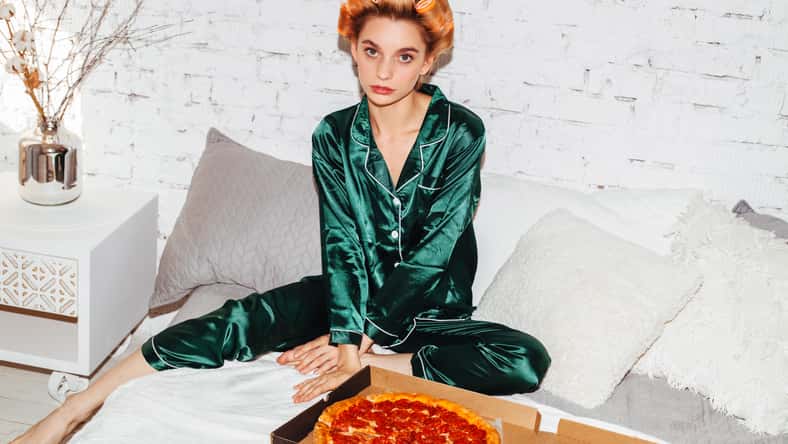 nice woman in pajamas doubting with pizza box in bed