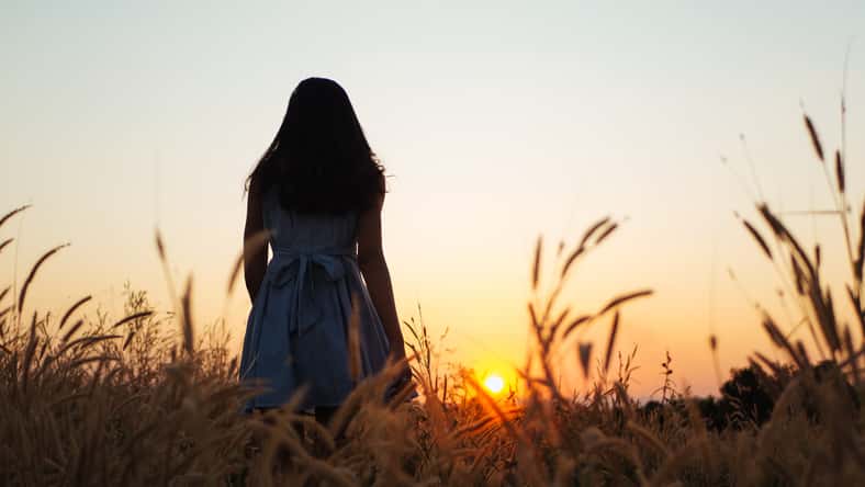 Trendy girl in stylish summer dress feeling free in the field with flowers in sunshine.