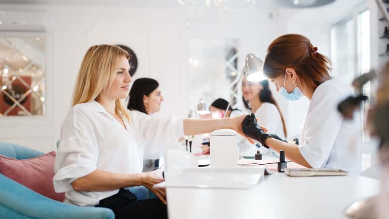 Group of girlfriends relax on manicure procedure in beauty salon. Professional beautician and female customers, nail care in spa, fingernail treatment