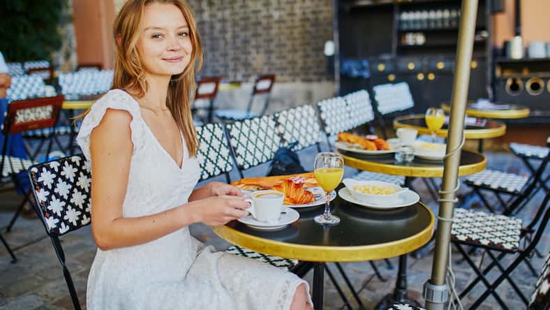 Cheerful young woman having breakfast or brunch in traditional French cafe on Montmartre in Paris, France