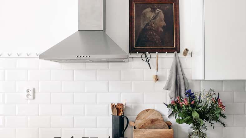 Interior de cocina ecléctica moderna. Muro de ladrillo blanco con baldosas de metro, rieles de clavija y pintura al óleo. Encimera de madera, campana de acero inoxidable y estufa de gas. Diseño escandinavo, puesta en escena, concepto.