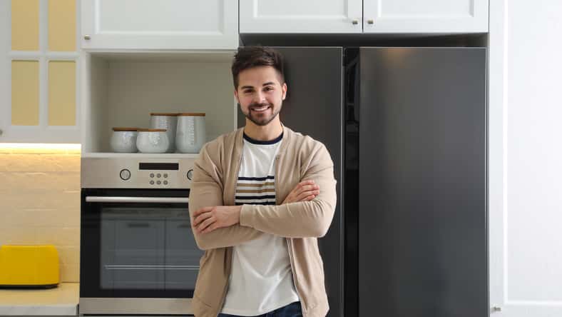 Happy young man near refrigerator in kitchen