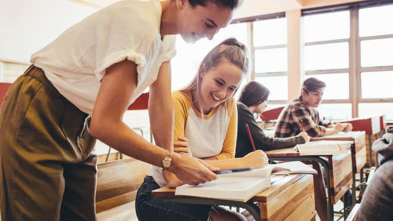 Happy female teacher assisting a teenage student in the classroom. Female professor helping girl student during a class at high school.