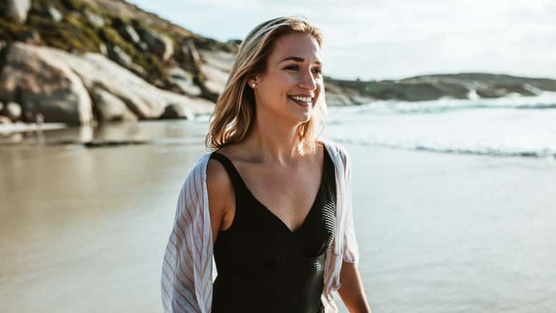 Woman walking along the sea shore. Female in swimwear walking on the beach.