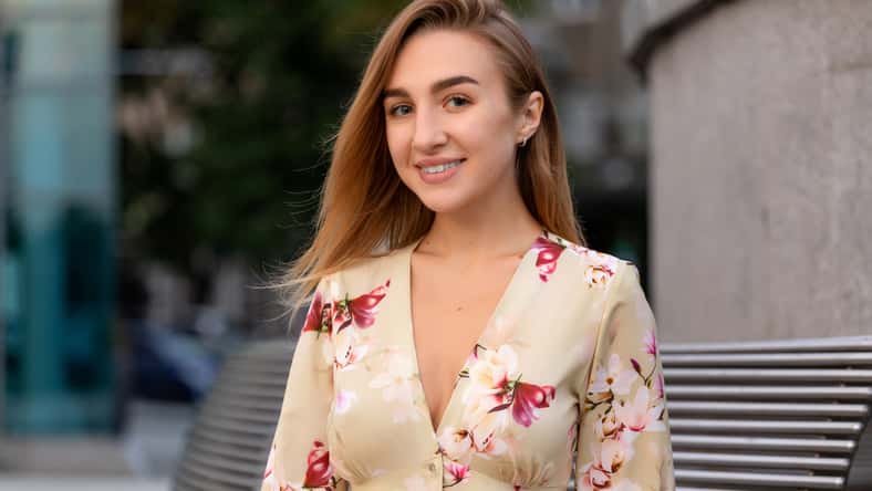 Portrait of a beautiful young girl on a background of a blue business center dressed in a summer beige dress