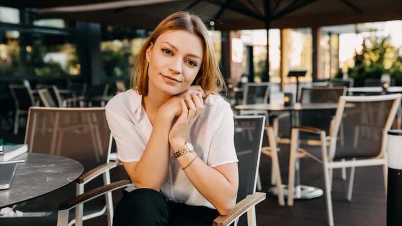 Young pretty woman, wearing a white shirt, looking to camera, smiling.