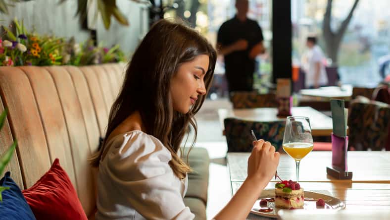 Beautiful young woman eating fruit cake alone at the restaurant