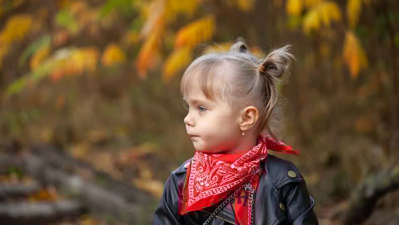 Closeup portrait of little girl turned head away from camera in autumn park.