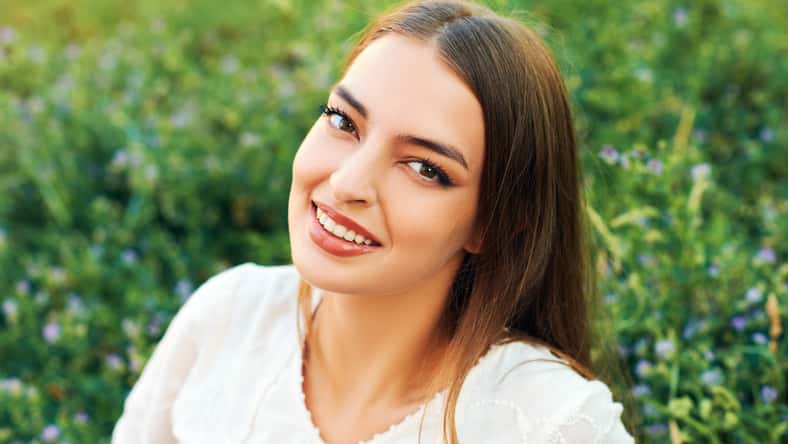 Fashion portrait of young woman resting on fresh green grass, wearing white dress