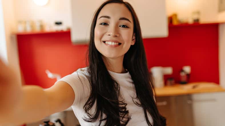 Woman in great mood takes selfie in kitchen. Portrait of brown-eyed girl