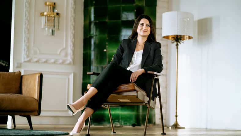 Sitting on a chair. Modern and stylish office. Illuminated by sunlight. Hardwood floors and a Vintage chair. Calm mood. The manager is a female student in a business suit of European appearance.