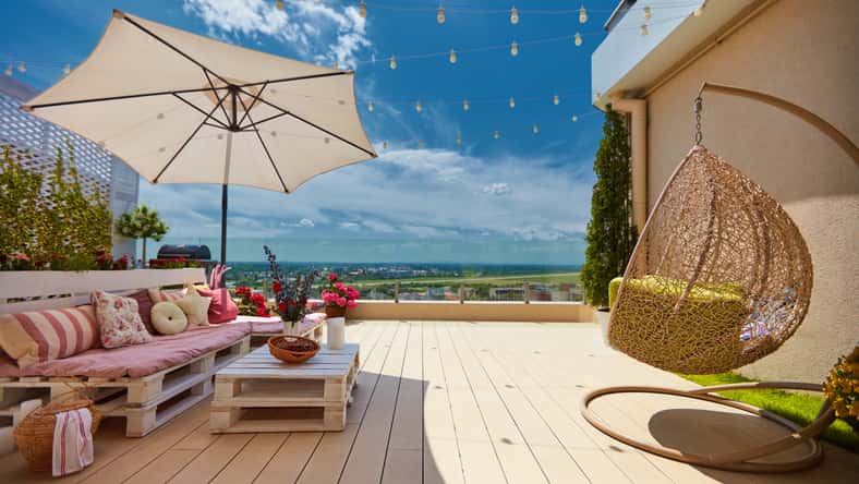 a cozy rooftop patio with wooden pallet furniture and hanging swing chair at sunny summer day