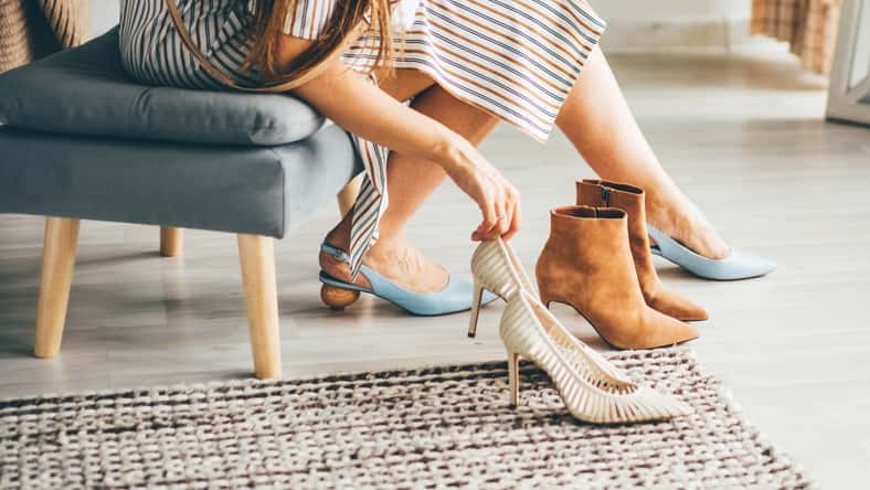 Fashionable young woman in striped dress trying new shoes while sitting on designed chair. Young woman changing shoes.