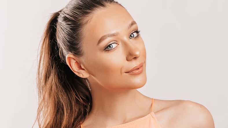 Hermosa joven sonriendo y posando mirando la cámara sobre un fondo blanco aislado. Mujer morena positiva. Mirada amable. Cara de belleza.