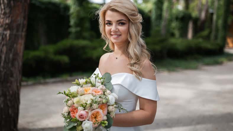 Smiling wedding couple in love in the forest hold hands and hug. Sunny day, good mood. Portrait of a beautiful blonde.