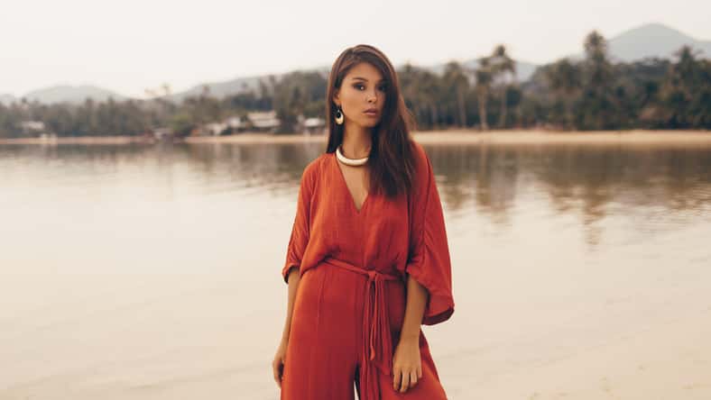 Asian woman in seductive red dress posing on the beach. Golden jewelry. Tropical island.