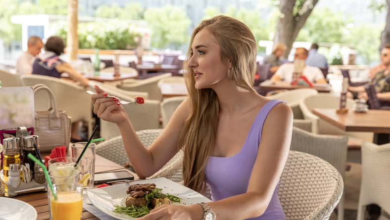 Beautiful young woman eating alone in the outdoor restaurant