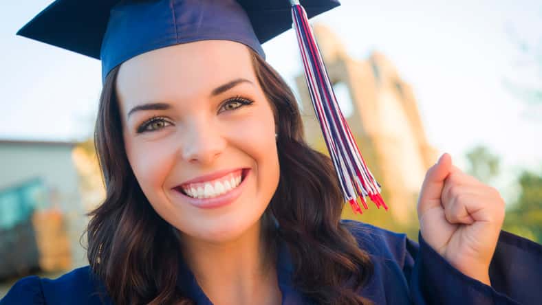 Happy Graduating Mixed Race Woman In Cap and Gown Celebrating on Campus.