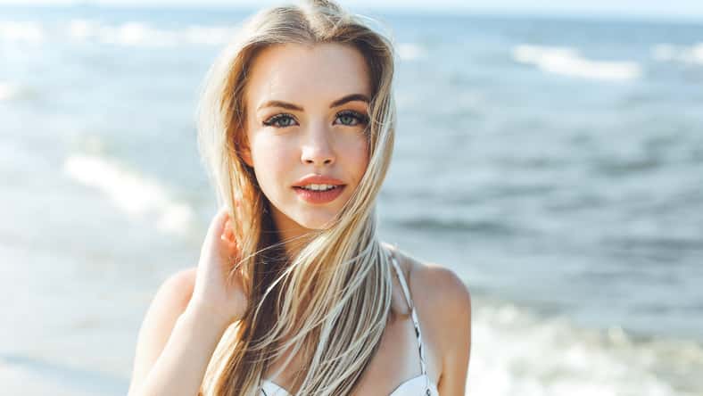 Happy blonde woman in free happiness bliss on ocean beach standing straight and posing.