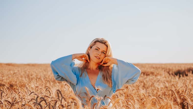 Beautiful adult blonde woman in summer in a field among ears of corn enjoys the warmth and fragrance of flowers - a portrait of a charming beauty