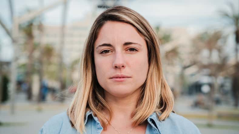 Individual close up portrait of serious young adult woman standing outside with pensive expression. Headshot of pretty confident female looking thoughtful at camera. Real formal lady staring front. High quality photo