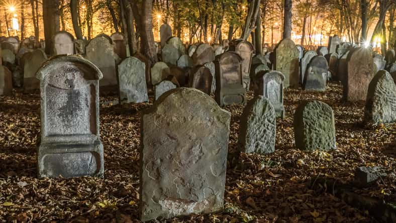 Lápidas en un antiguo cementerio por la noche en otoño. Las lápidas cubiertas crean una escena espeluznante. Las lápidas inclinadas se suman al ambiente misterioso. Las lápidas espeluznantes de las tumbas envejecidas se encuentran en medio de árboles en el cementerio.