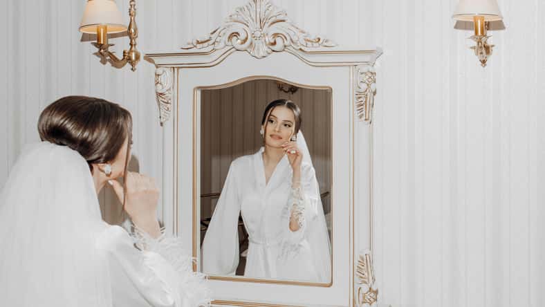 Portrait of a young beautiful bride in a beautiful hotel interior preparing for her wedding. A gorgeous woman looks in the mirror at her makeup and hairdo