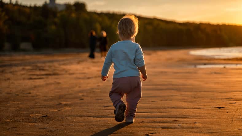 Little baby child toddler walks along an empty beach by the sea at sunset alone, calm and relax, active childhood