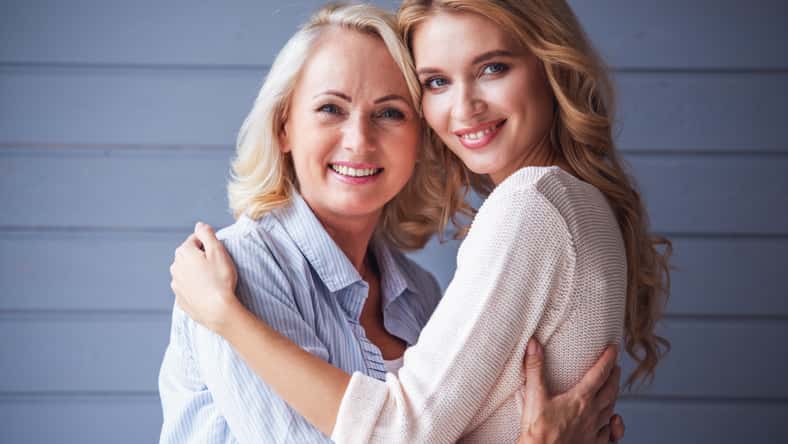Beautiful senior mom and her adult daughter are hugging, looking at camera and smiling