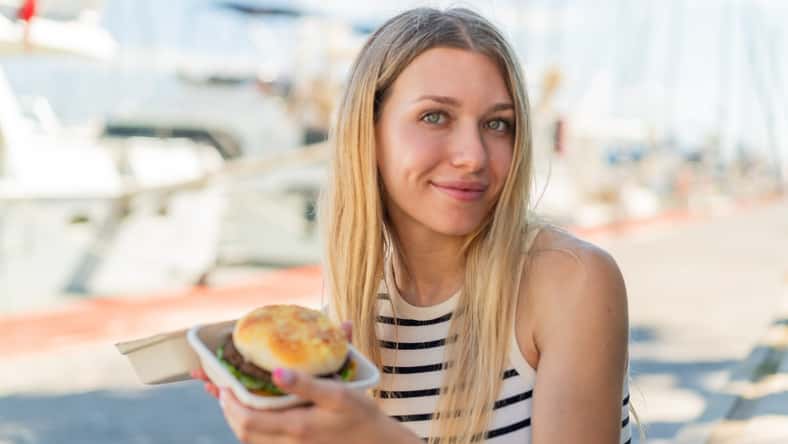 Young blonde woman at outdoors holding a burger