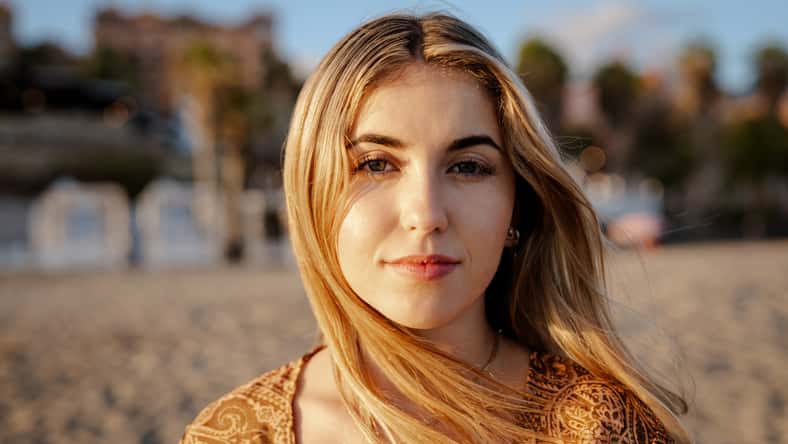 Portrait of one young, beautiful woman on the sand of the beach enjoying and relaxing at the sunset of the day. Looking at the camera serious.