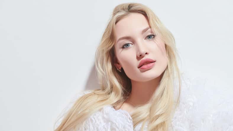 Portrait of a beautiful young woman with blonde hair and sensual lips posing in a fluffy white fur coat on a white studio background. Beauty care cosmetics. Cosmetology.