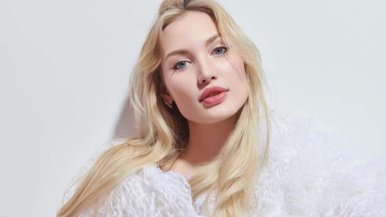 Fashion Shoot. Hermosa mujer joven con cabello rubio y labios posa en un esponjoso abrigo de piel blanca sobre un fondo de estudio blanco. Cosméticos de cuidado de belleza.