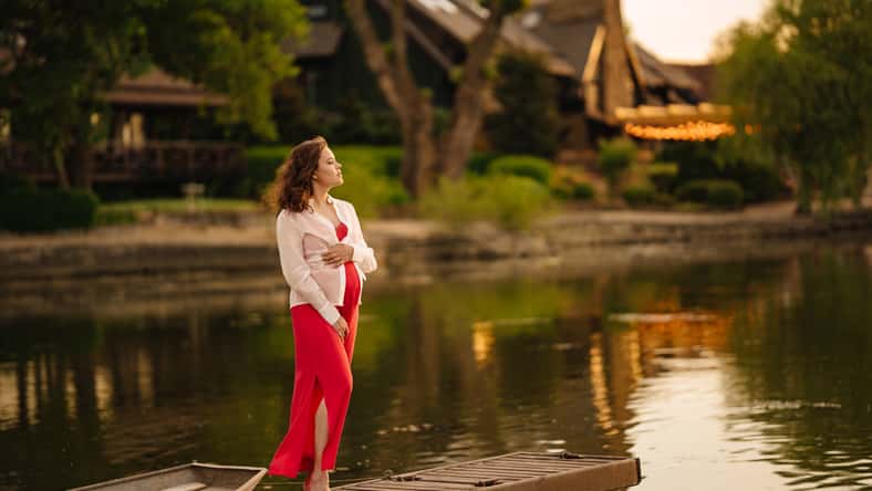 Beautiful young pregnant woman in red dress at sunset on the riverbank. Beautiful and comfortable clothes for pregnant women. happiness and comfort of waiting for the birth of a baby.