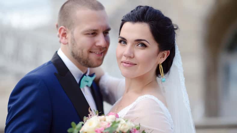 Wedding couple on the nature is hugging each other. Beautiful model girl in white dress. Man in suit. Beauty bride with groom. Female and male portrait. Woman with lace veil. Lady and guy outdoors