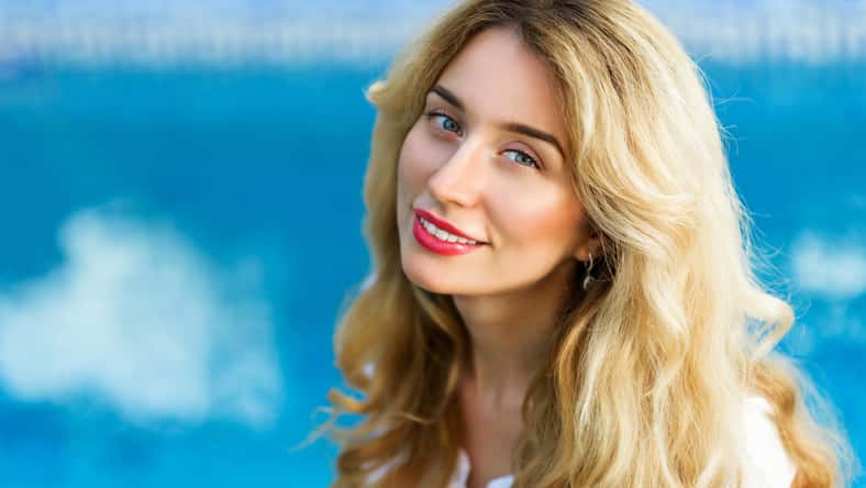 Happy young woman smiling. Curly blonde hair and red lips. Blue Background