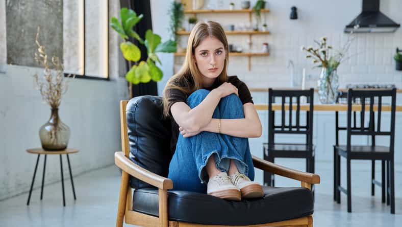 Portrait of young beautiful woman, serious college university student looking at camera sitting at home in chair. Attractive female blonde, lifestyle, youth concept