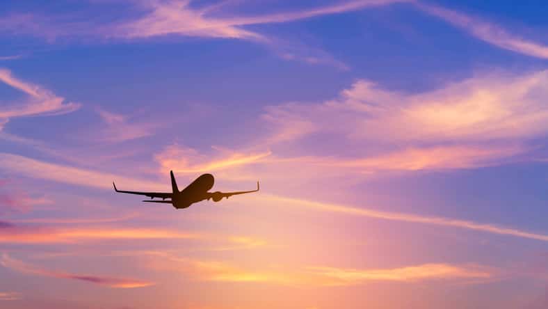 Silhouette passenger airplane flying away in to sky high altitude above the sun during sunset