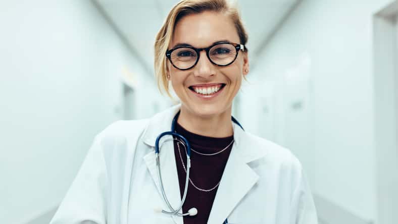 Portrait of happy young female doctor standing in hospital corridor. Caucasian woman working in healthcare center.