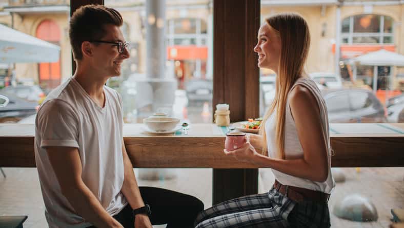 Happy young couple in love having a nice date in a bar or restaurant. They telling some stories about themself , drinking tea or coffee and and eating salad and soup