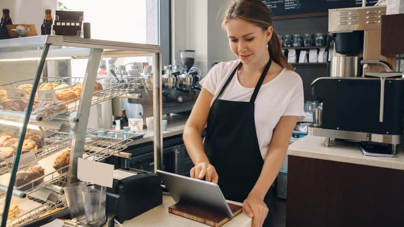 Portrait of young caucasian female woman cashier. Seller using touch pad for accepting client customer payment. Small business of coffee shop cafeteria.