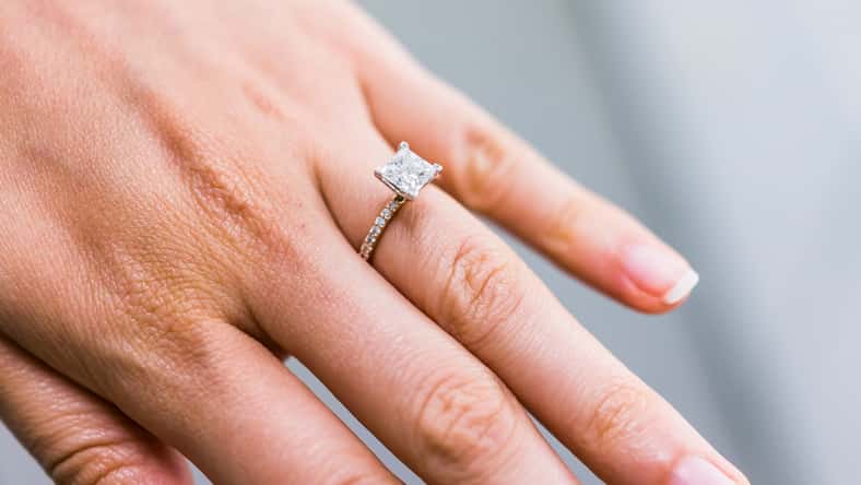 Macro closeup of princess cut diamond engagement ring on woman's female hand showing detail and texture