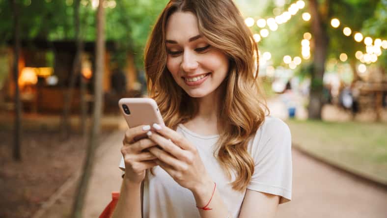 Smiling young girl holding mobile phone while standing at the park