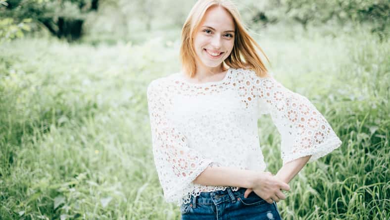 Beautiful attractive young woman posing in spring park wearing white knitted top and blue jeans, modern creative toning
