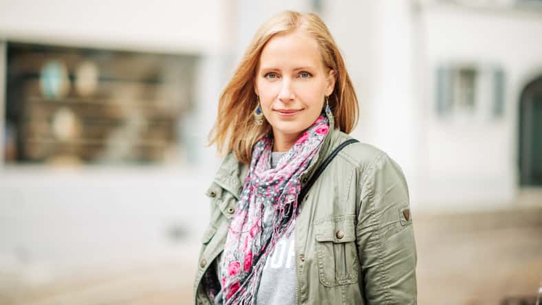 Outdoor portrait of beautiful blond woman, posing outdoors, wearing khaki color parka and pink scarf