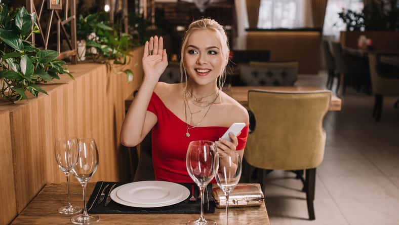 attractive woman in red dress sitting in restaurant waving hand