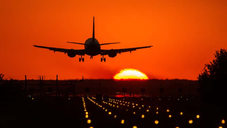 Silhouette of air plane landing on illuminated track at sunset with beautiful red sky and sun in background